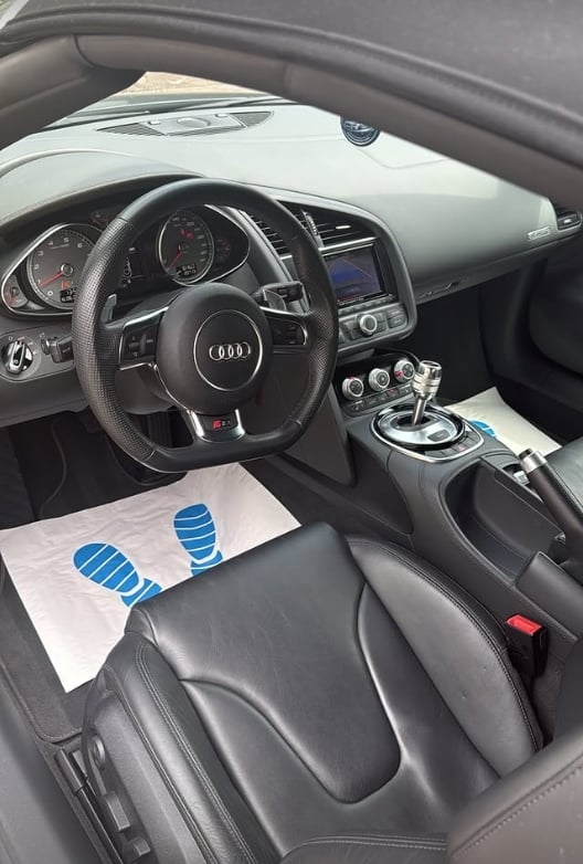 Interior view of Audi sports car with black leather steering wheel and blue footprints on floor mat