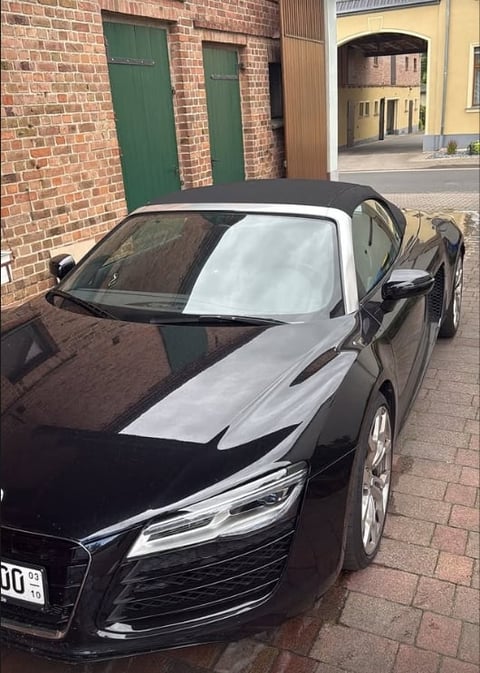 Black sports car parked on brick courtyard with white sunshade