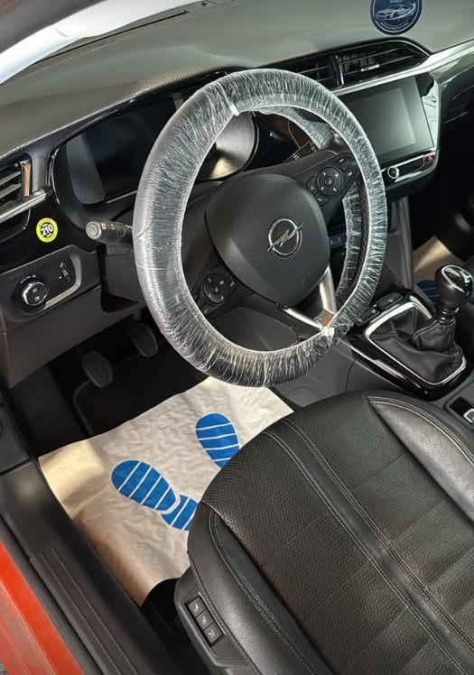 Car interior showing steering wheel with plastic protective cover and seat covered with packaging material